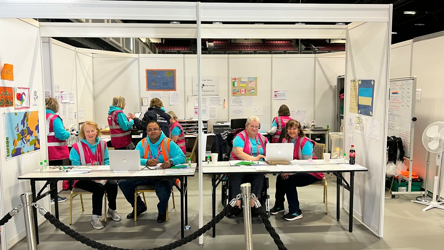 Volunteers staff an information desk while working on laptops.