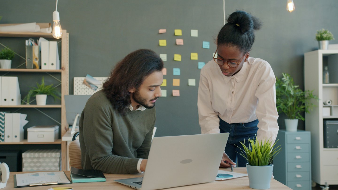 Two professionals collaborating over documents and laptop at a desk.